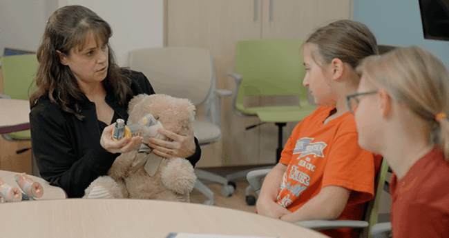 HowToUseAnInhaler_Featured adult using teddy bear prop while speaking with two young girls