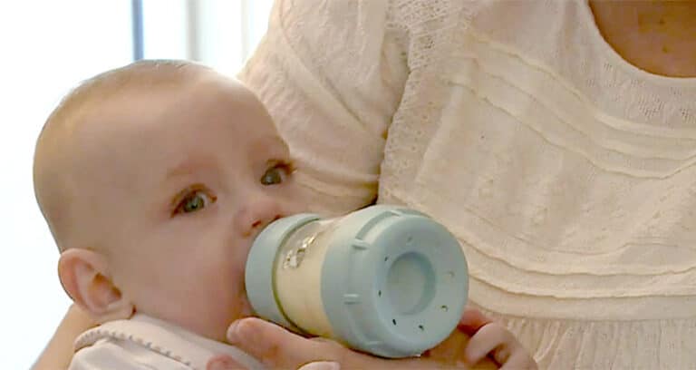infant drinking from a bottle while being held