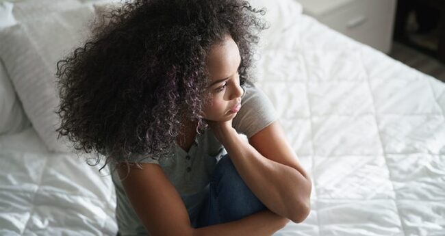 ChildrensHealth_20220222_MoodyTeen Black teen sitting on bed looking anxious