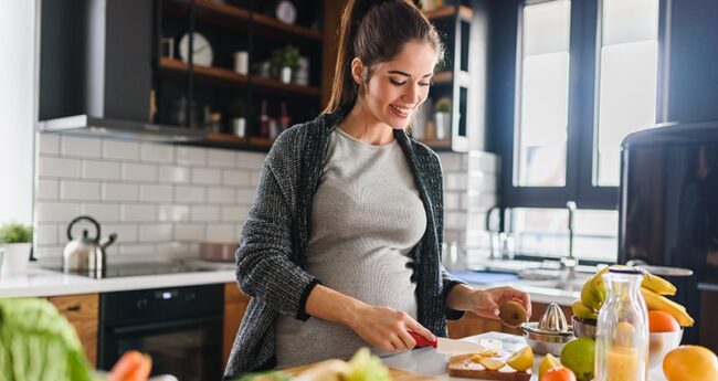 WomensHealth_2022-0325_EatingWellDuringPregnancy pregnant woman cutting fruit in a kitchen