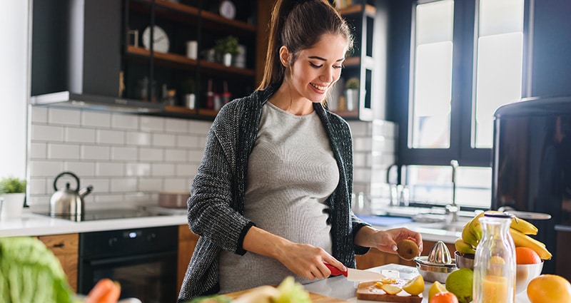 pregnant woman cutting fruit in a kitchen