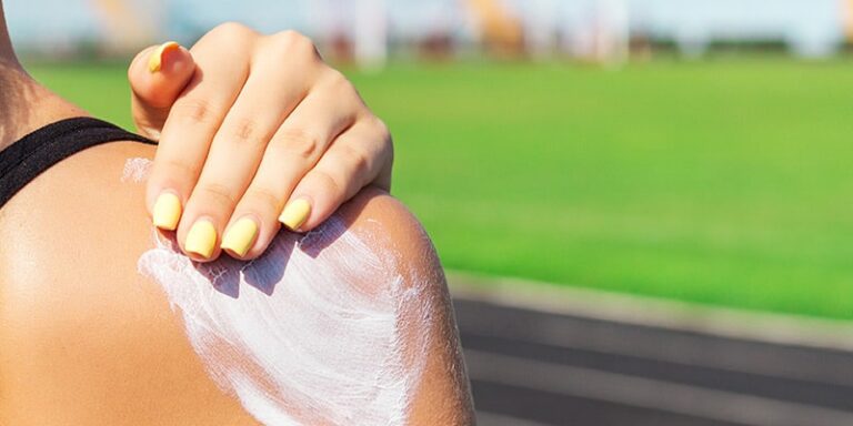 woman rubbing sunblock into shoulder in front of green field
