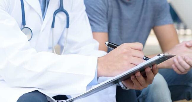 monkeypox medical professional filling out paperwork on a clipboard while sitting next to patient