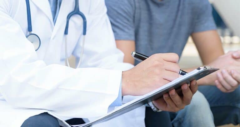 medical professional filling out paperwork on a clipboard while sitting next to patient