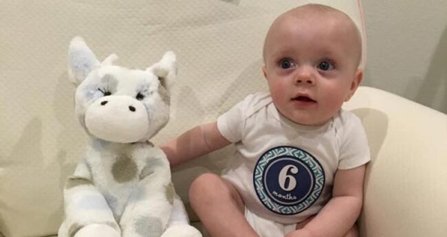 infant sitting enxt to stuffed cow toy