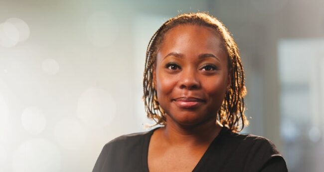 A woman wearing a black suit is shown against a sunny background