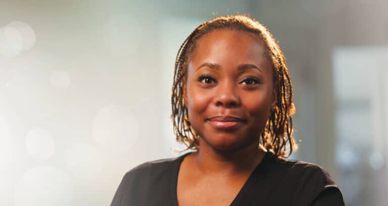 A woman wearing a black suit is shown against a sunny background