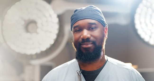 A smiling, bearded man wearing scrubs
