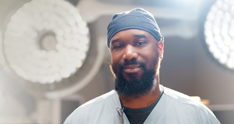 A smiling, bearded man wearing scrubs