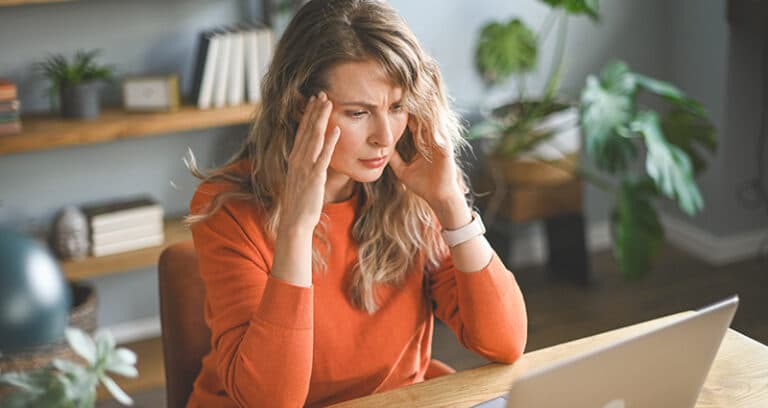 woman rubbing forehead looking at a computer