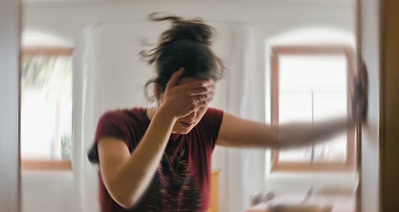 woman holding her head and leaning against doorframe