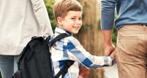 child smiling over shoulder while holding two adults' hands