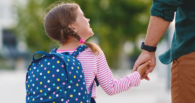 Girl in striped pink shirt and pigtails looking up and smiling at man whose hand she's holding