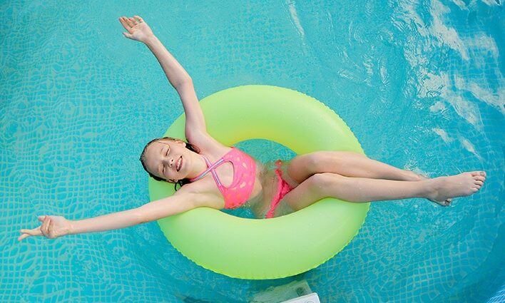 girl floating in pool in bright pink bathing suit
