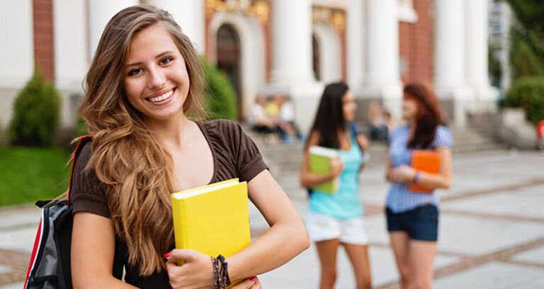 female college student smiling in foreground with two others talking in background