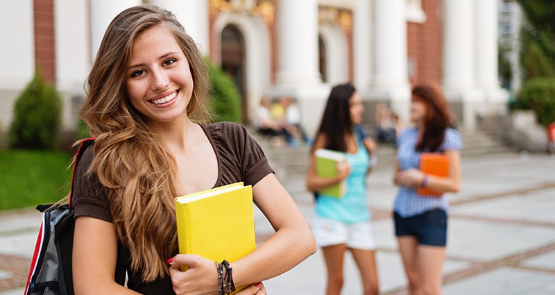 female college student smiling in foreground with two others talking in background