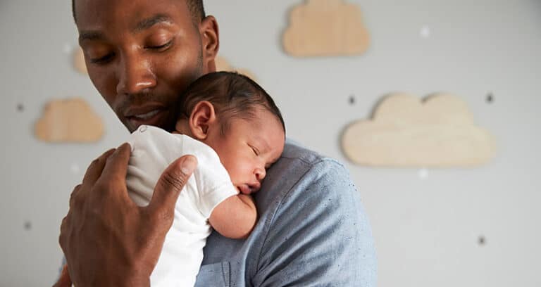 infant being held on adult man's shoulder