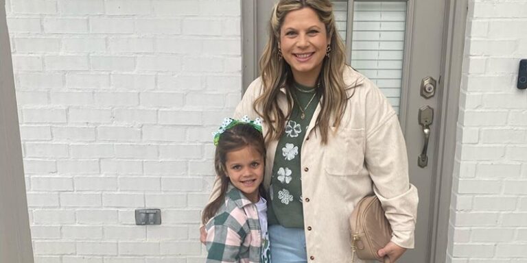 A woman and a little girl stand in front of a doorway. They are smiling.