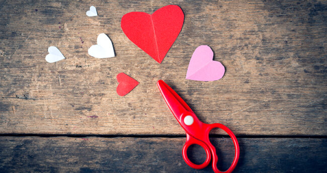 Scissors and construction paper hearts on wooden background
