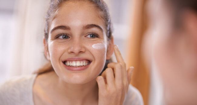 Tween adding skin care as she looks in a mirror