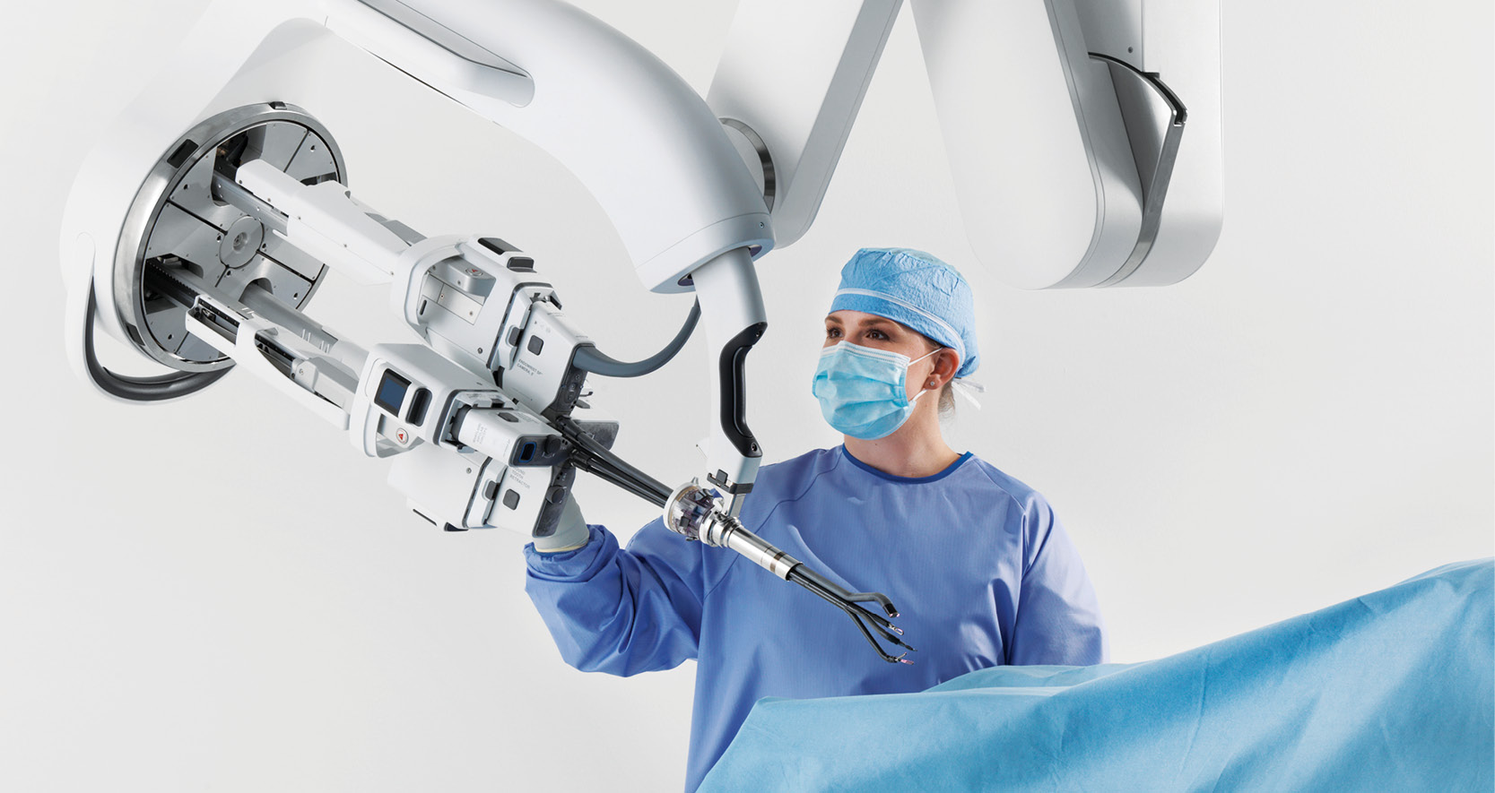 A surgeon wearing blue scrubs and a mask working with a surgical robot