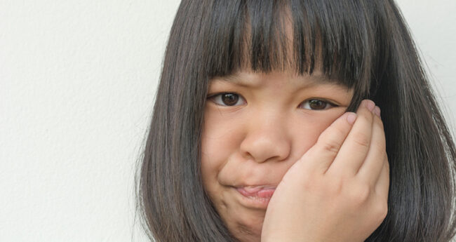 Child holding her cheek with a grimace